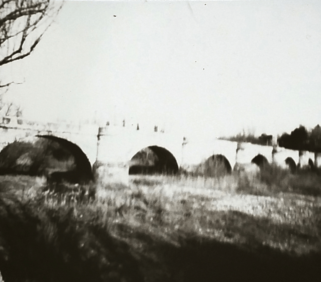 Foto en blanco y negro de un puente antiguo de piedra sobre el lecho de un río