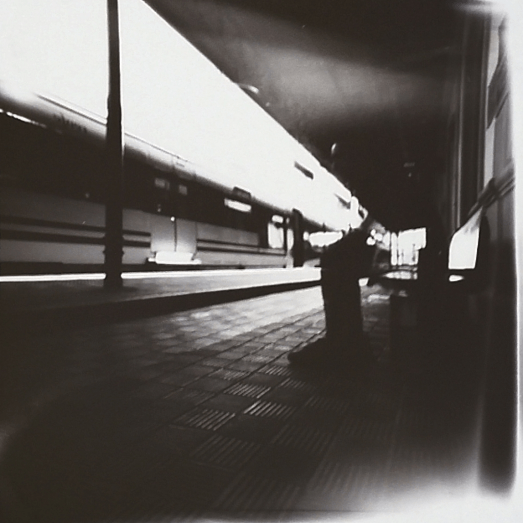 Hay un hombre sentado en un banco de una estación de tren. Frente a él, un tren con las puertas cerradas.